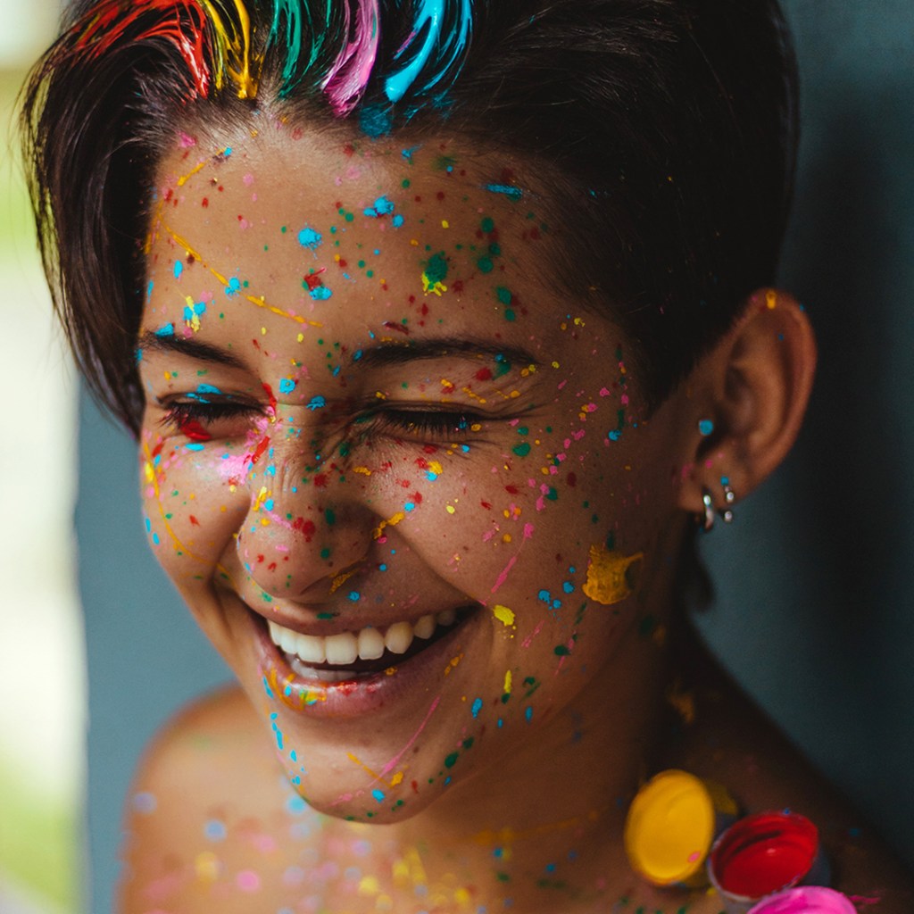Happy dancer smiling with rainbow paint on face. 