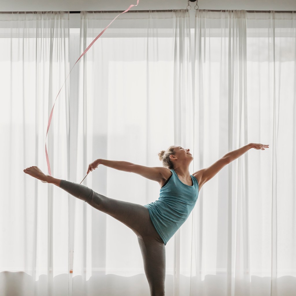 Ribbon dancer at yoga studio with pink ribbon performing arabesque.